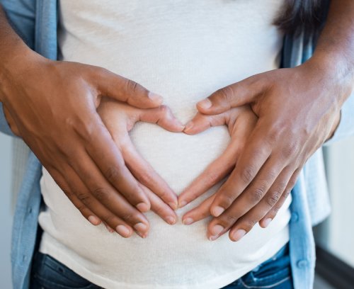 Photo of two hands making a heart shape on a pregnant stomach