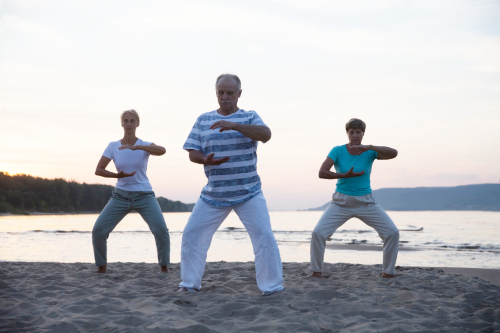 photo of 3 older adults doing qi gong on a beach during sunrise