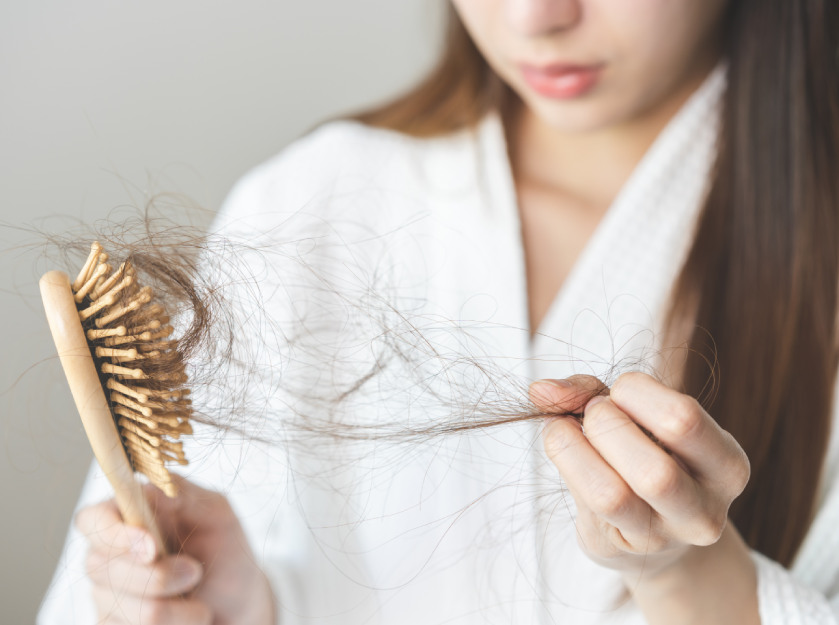 photo of a woman holding a hairbrush ful of hair that has presumably fallen out