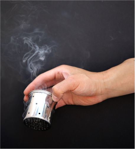 Photo of a hand holding a smoking moxa pot